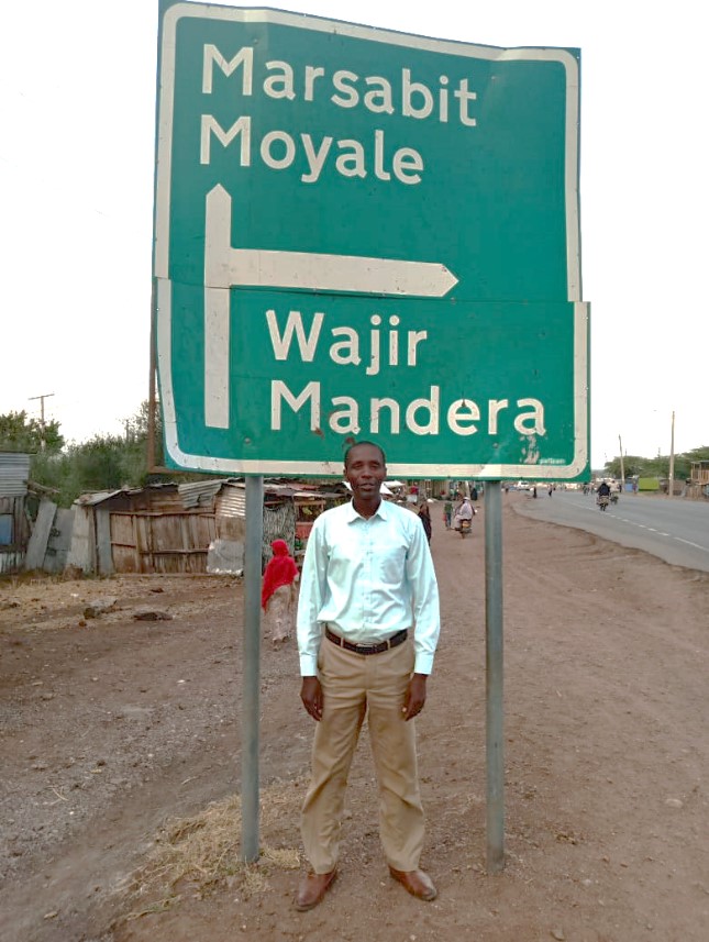man standing in front of road sign in kenya