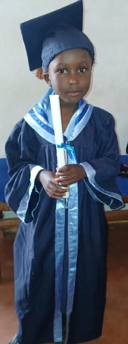 an image of talia in her kindergarten graudation gown and cap with her certificate in her hands